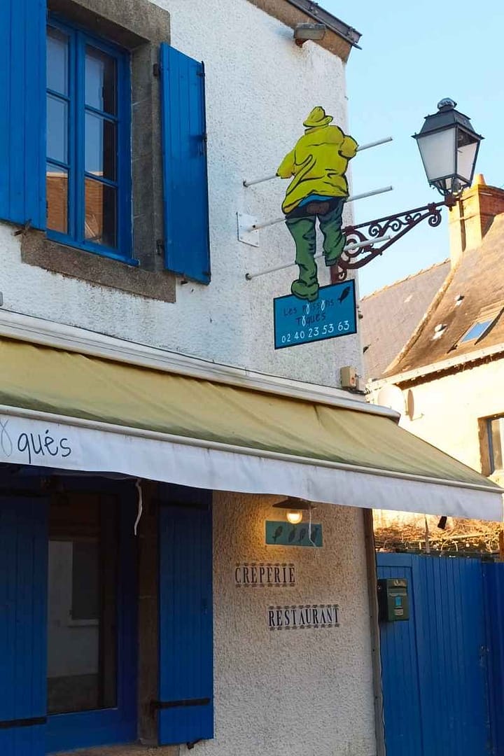 Balades & Randonnées avec son chien : applique représentant un marin avec son ciré jaune sur la façade d'une crêperie vu lors d'une balade avec mon chien à Piriac-sur-Mer