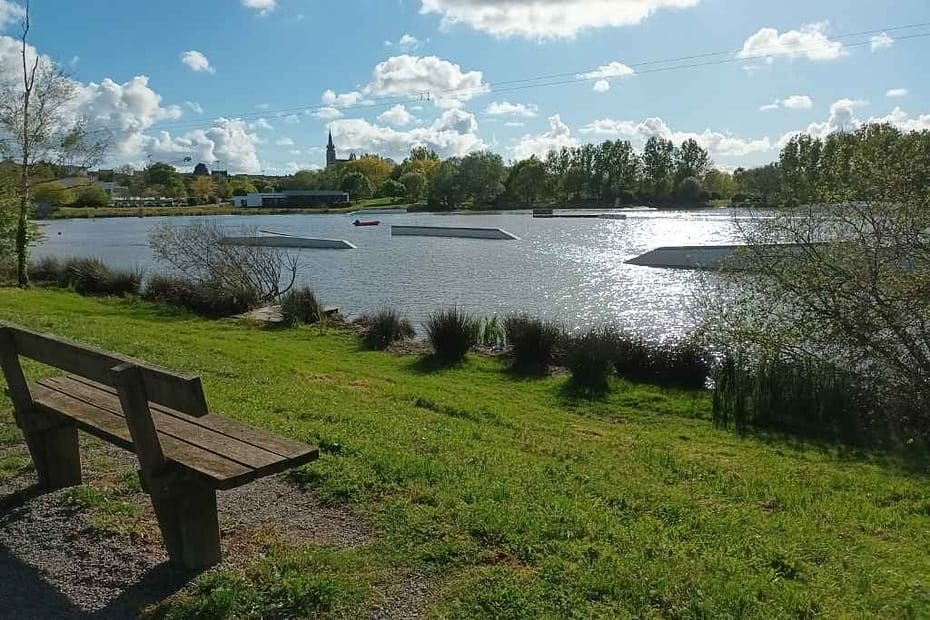 Balades & Randonnées avec son chien : vue sur un banc en bois donnant sur le lac Saint-Viaud en Loire-Altantique avec en second plan le clocher de l'église